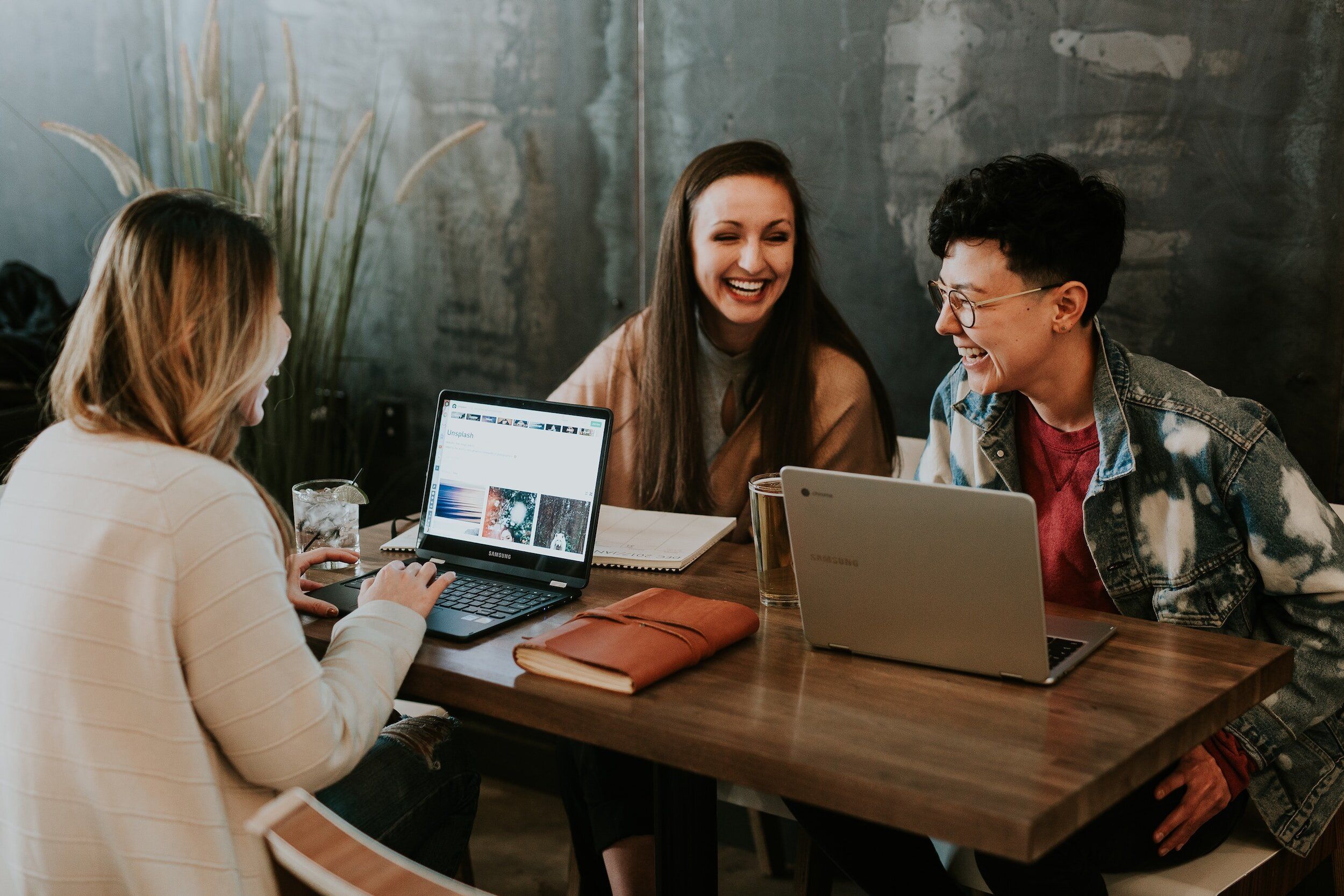 Three people laughing together around a table with laptops